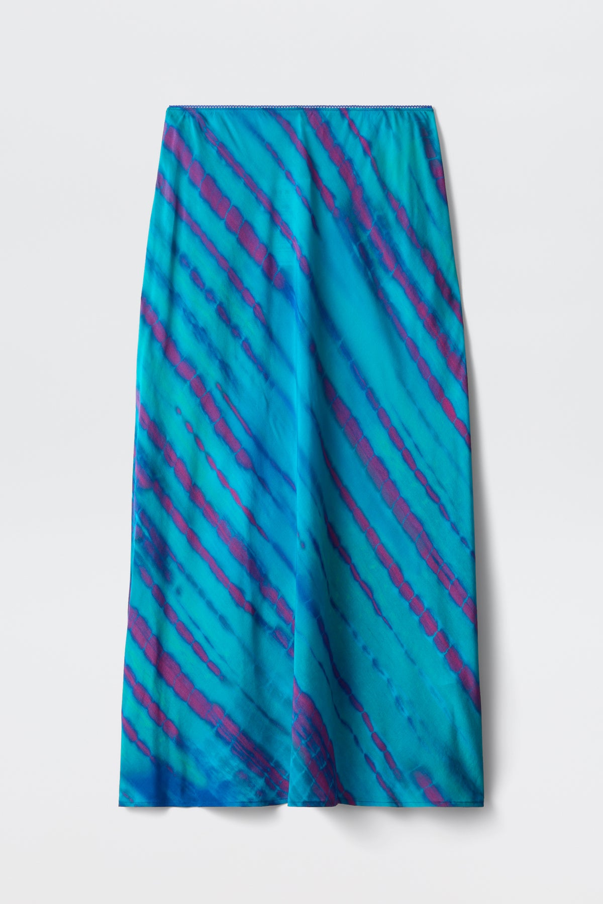 The Ardith - Tie Dye Blue is a long, straight skirt with a vivid blue base and diagonal tie-dye stripes in purple and deep blue, displayed flat against a plain white background.