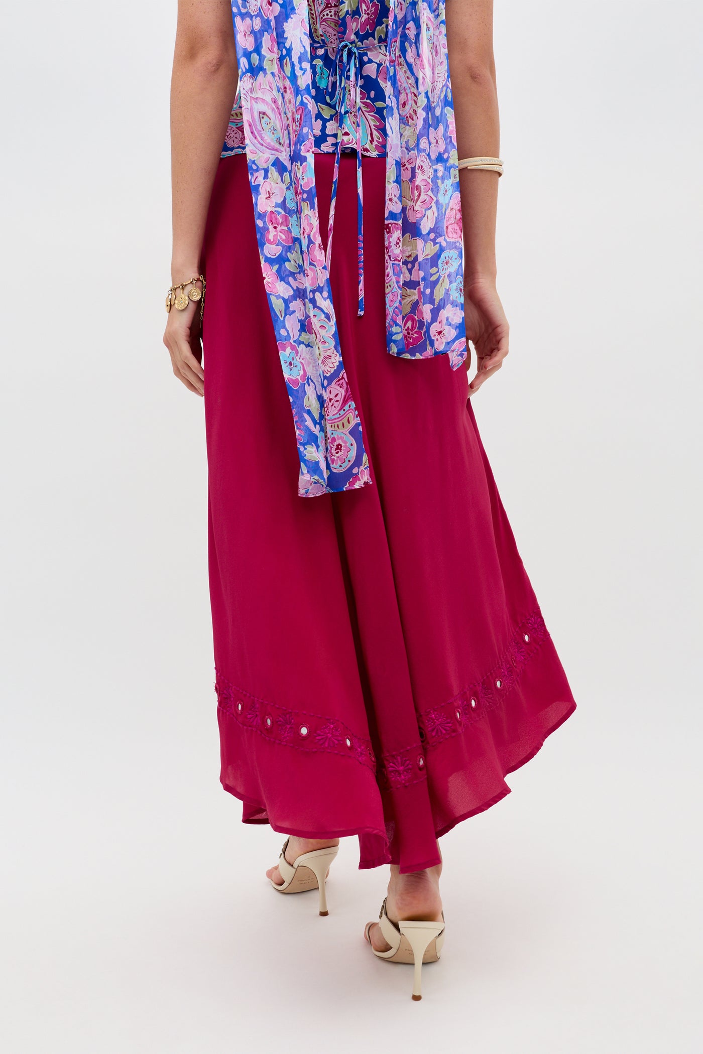 A person wearing the “Rudy - Mirror Embellishment Magenta Pink” skirt, beige heels, a blue floral top, and gold jewelry, standing against a plain light background.
