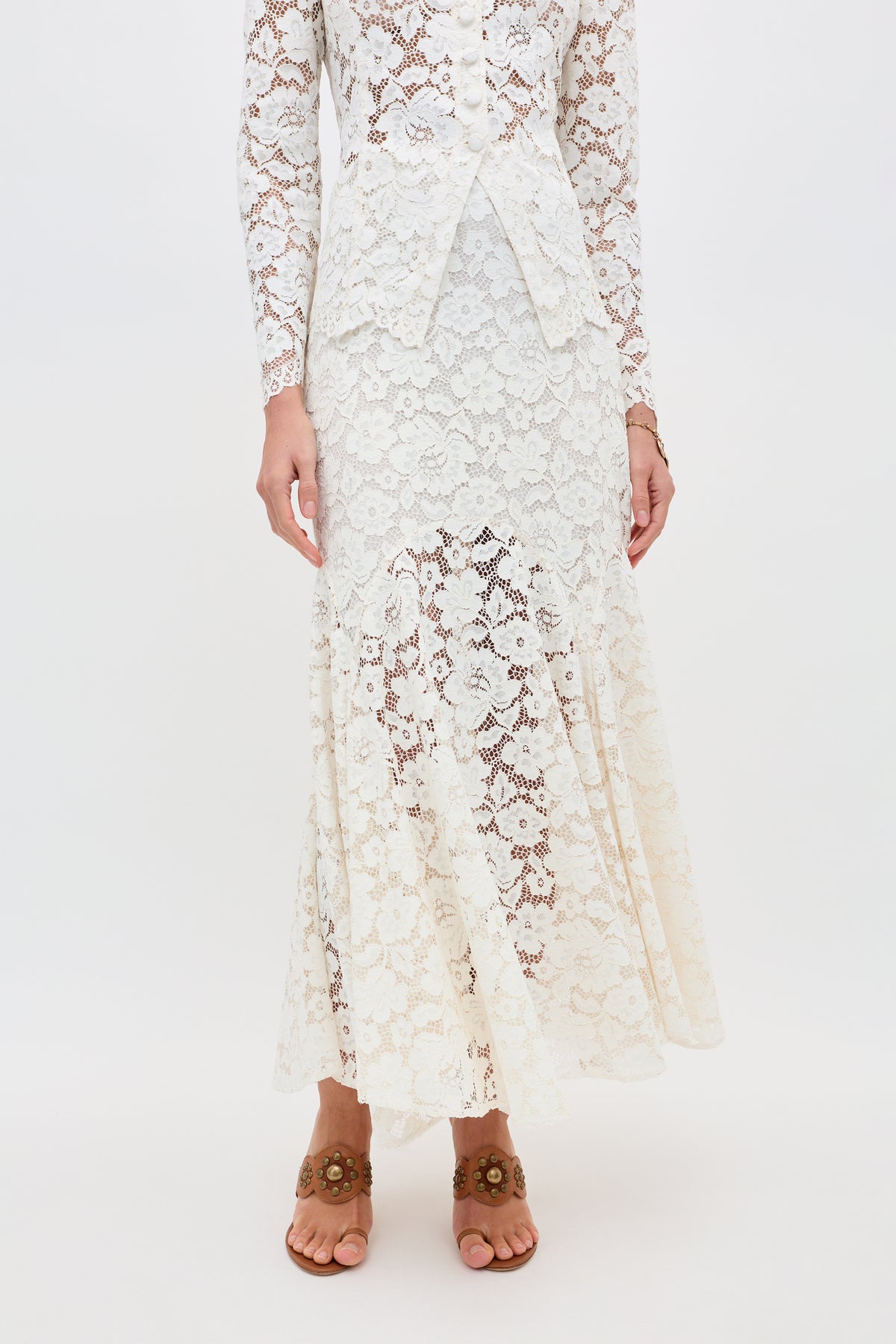 A person wearing the Jada - Cream long-sleeved lace dress with a fitted waist and flared hem stands barefoot on tiptoe, hands relaxed at their sides, against a plain white background.