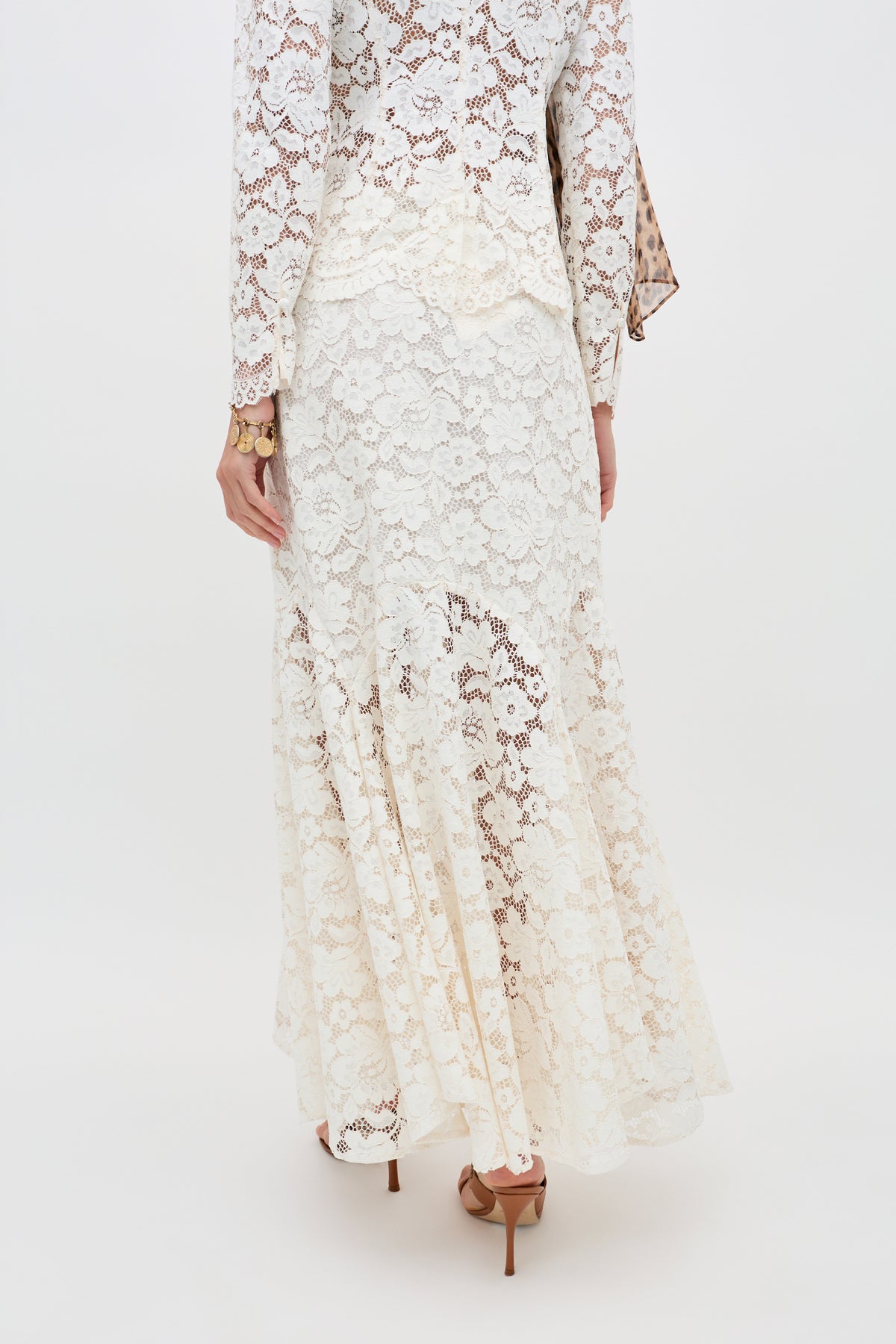 A person wearing the Jada - Cream long, white lace dress with long sleeves and light brown high-heeled sandals, shown from the back against a plain light background.
