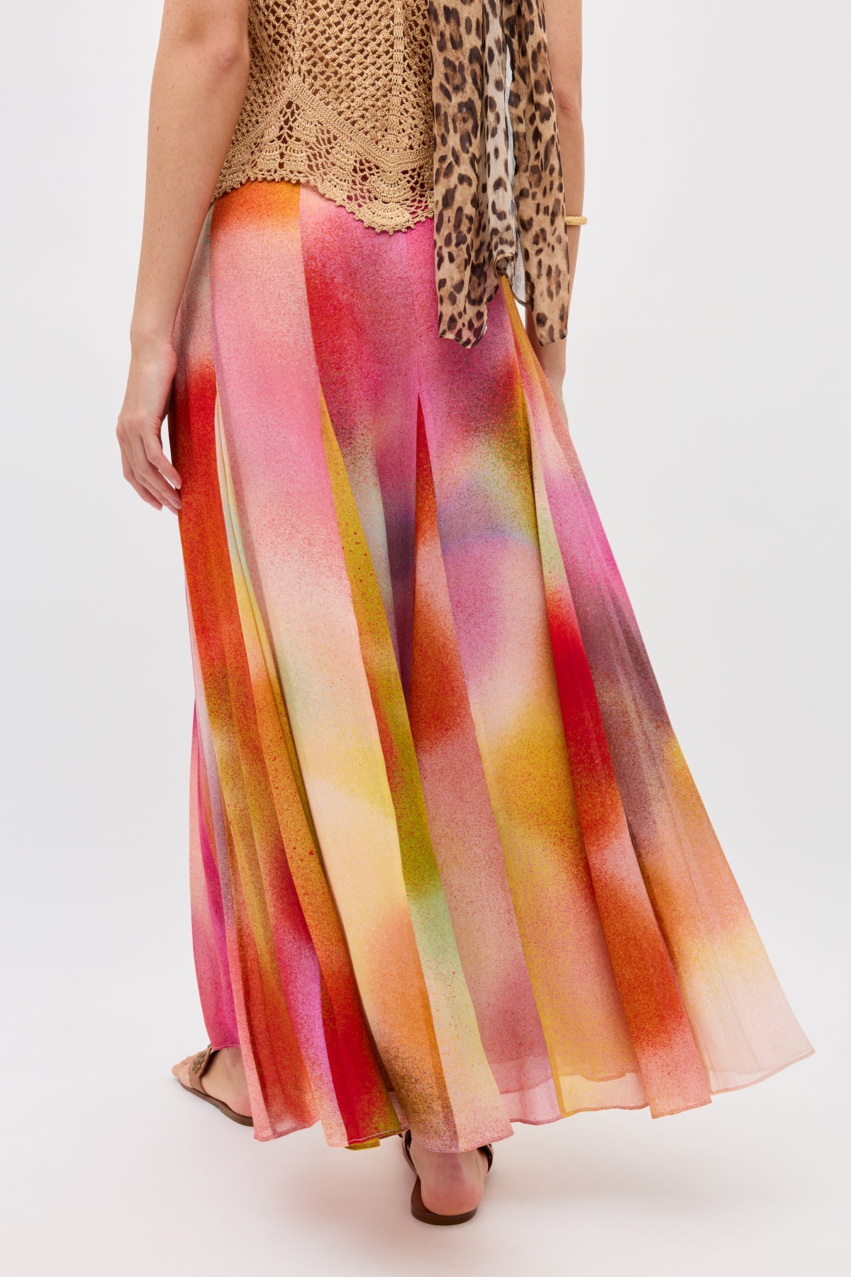 A person wears the Billy - Jessica Alexandra Multi—a colorful, flowing maxi skirt with abstract pink, orange, yellow, and green patterns—paired with a tan crochet top and leopard-print scarf. Image is from behind against a plain background.
