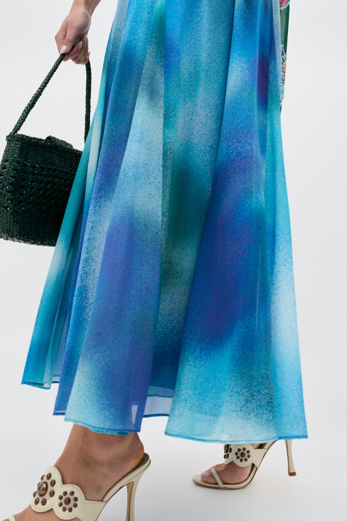 Wearing the Billy - Jessica Alexandra Blue flowing dress in Liberty fabric, paired with cream high-heeled sandals featuring flower cutouts and a dark green woven handbag—perfect for effortless spring and summer style.