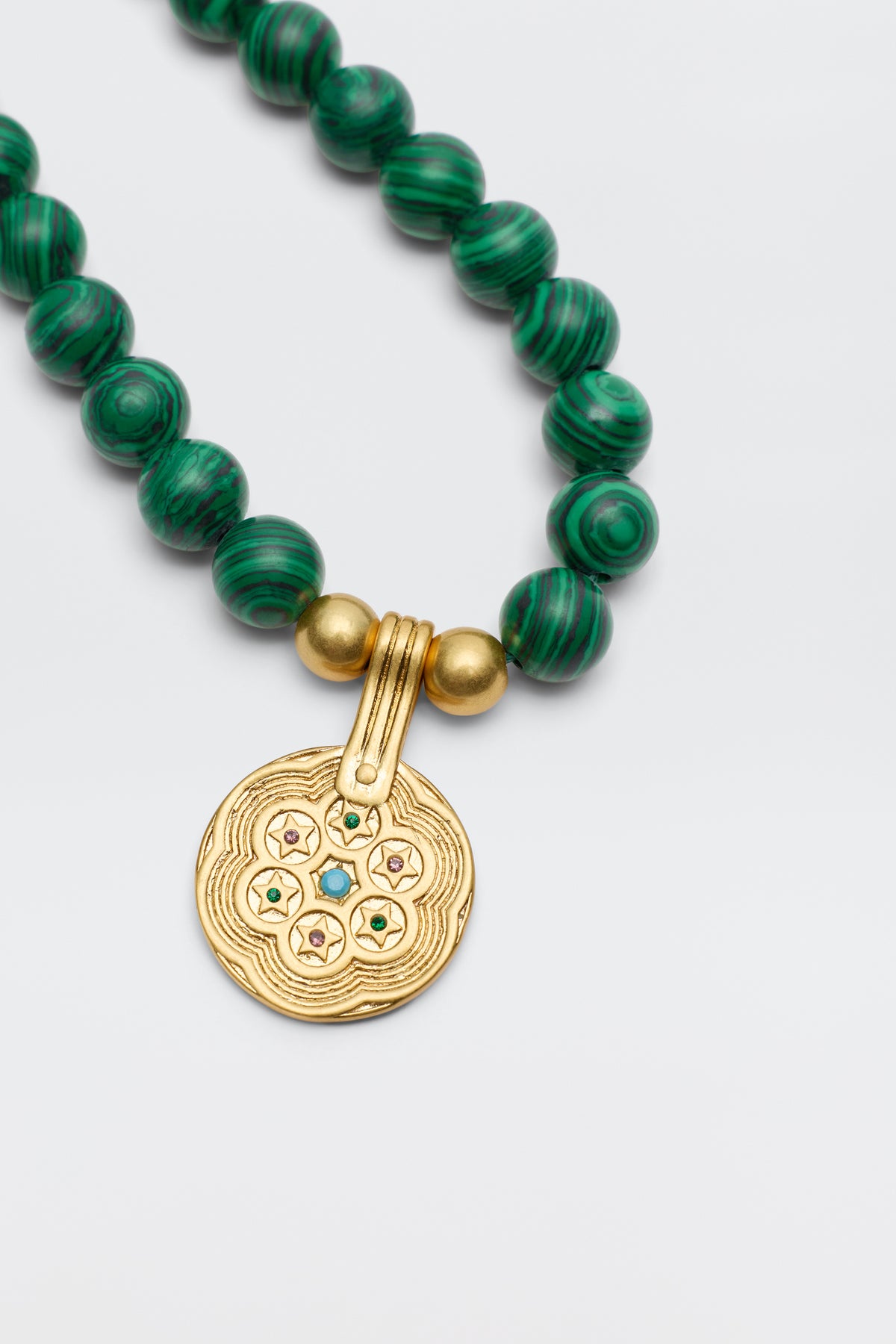 Ischia - Green: A necklace with round, marbled green beads and a large gold pendant engraved with wavy lines and small motifs, featuring five tiny malachite crystals in delicate star-shaped settings.