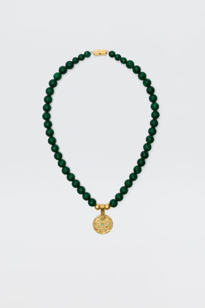 The Ischia - Green necklace features round dark green malachite beads with a gold clasp and an engraved golden pendant, displayed on a plain white background.