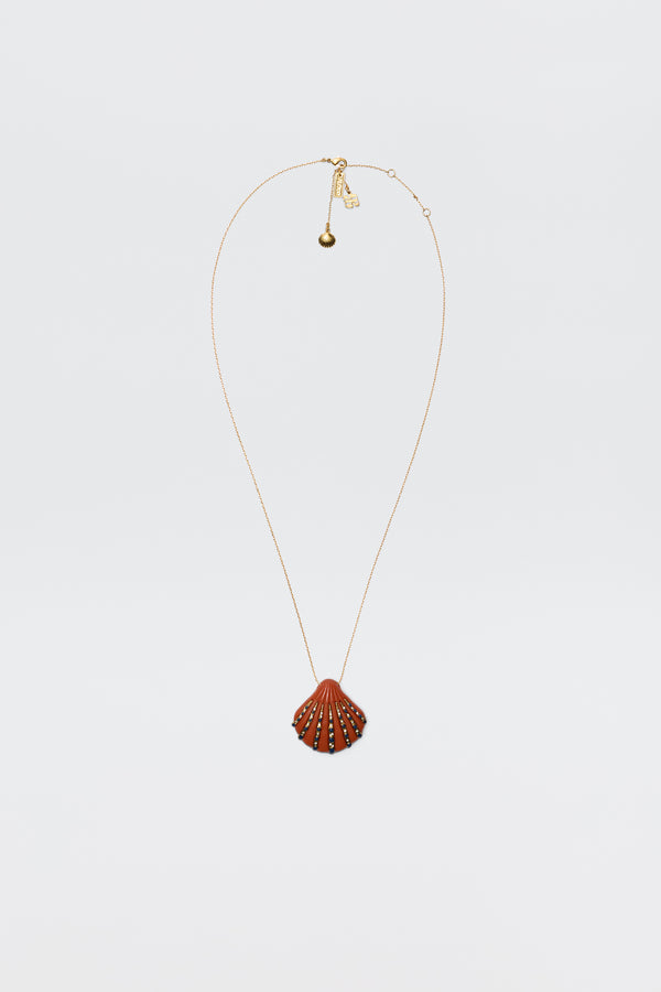 The Leanira - Orange necklace features a scallop shell-shaped pendant with small decorative studs on a gold-plated chain, shown against a plain white background.