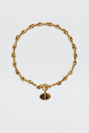 The Zandra - Gold features a chunky, vintage-inspired gold-plated chain with twisted links and an oval dark brown gemstone pendant set in a gold frame, shown against a plain white background.