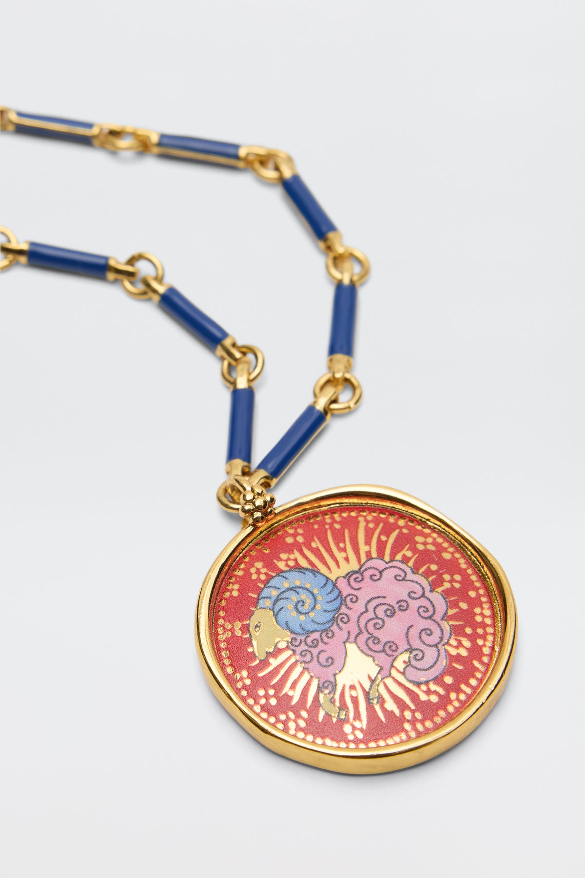 The Ari - Astro Aries necklace features a gold zodiac pendant with a stylized ram on a red background, blue and purple curls, gold accents, and bold blue chain links.