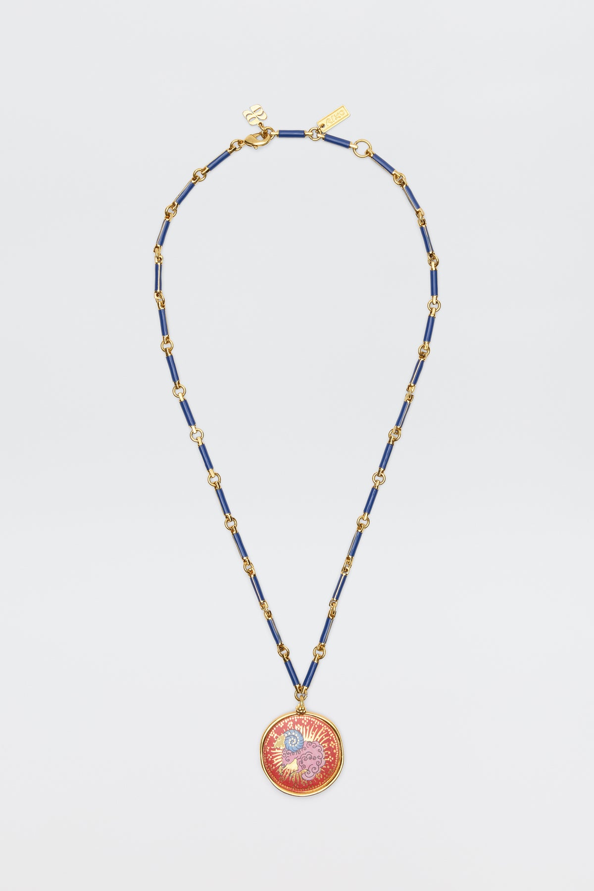 The Ari - Astro Aries necklace features a gold and blue chain with a circular red and gold sunburst pendant, displayed on a plain white background.