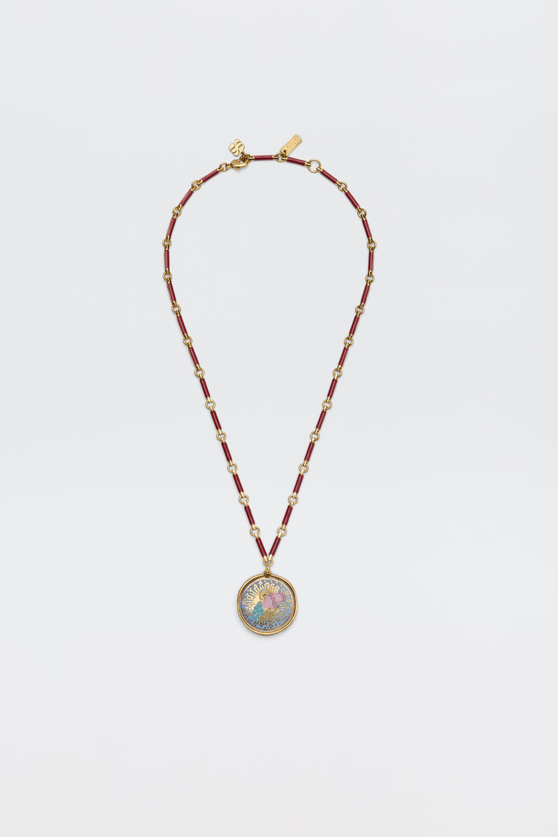 The Ari - Astro Aquarius necklace features gold zodiac detailing, red cylindrical beads, small gold spacers, and a statement disc charm with a colorful, intricate design at the center. Displayed against a plain white background.