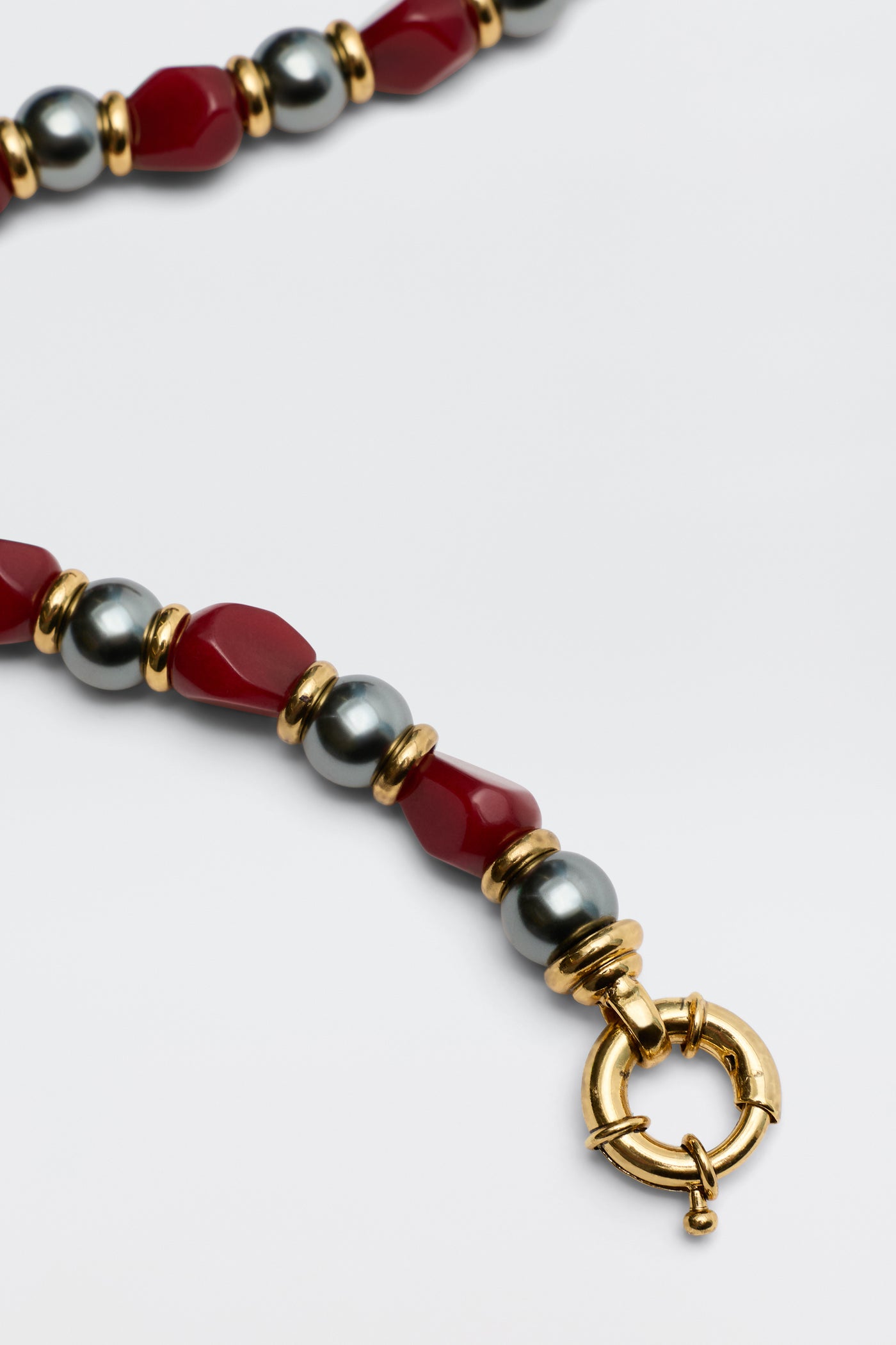 A close-up of the Palmara - Burgundy necklace, showcasing alternating red and metallic grey beads with gold accents and a round gold clasp on a plain white background.