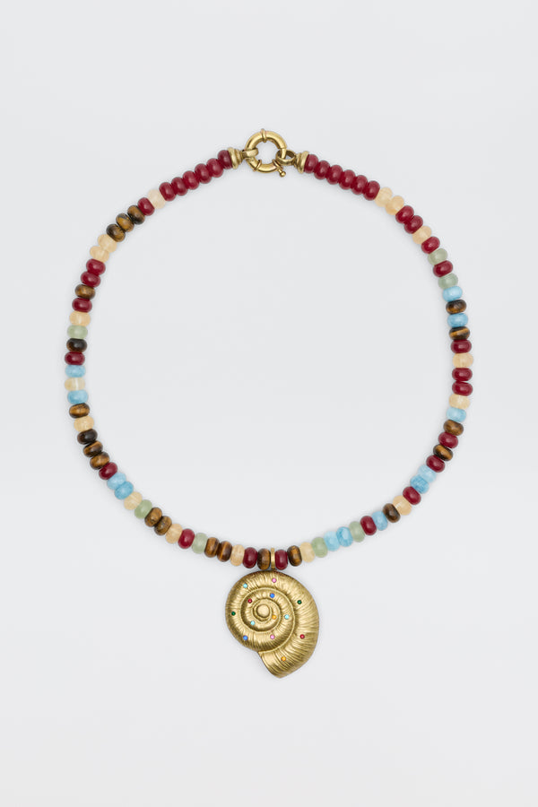 The Parma - Multi beaded necklace showcases red, blue, brown, and white beads with a gold spiral shell pendant adorned with small colored gemstones, elegantly displayed on a white background.