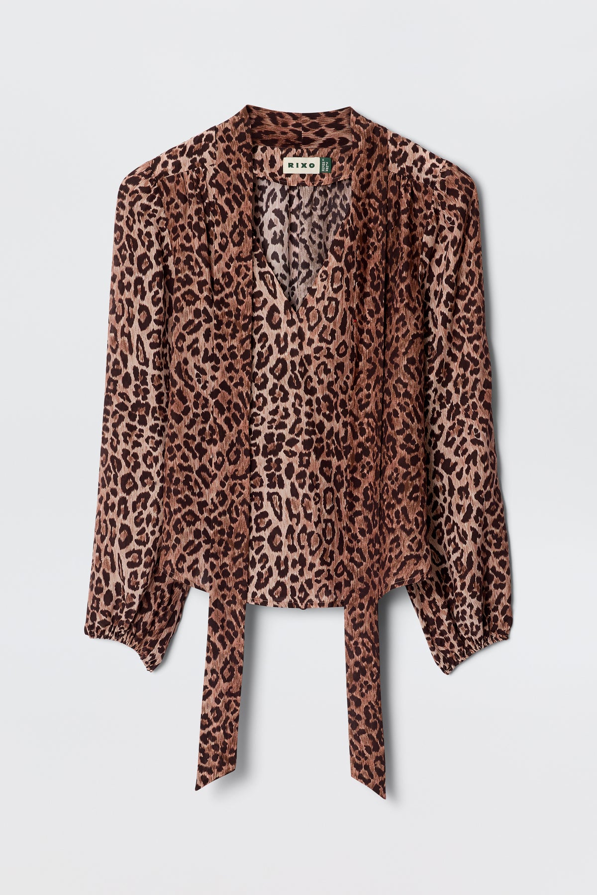 The Moss - Leopard Brown blouse features long sleeves, lightweight leopard-print silk, a V-neck, and front tie details, displayed on a plain light background for a vintage-inspired look.