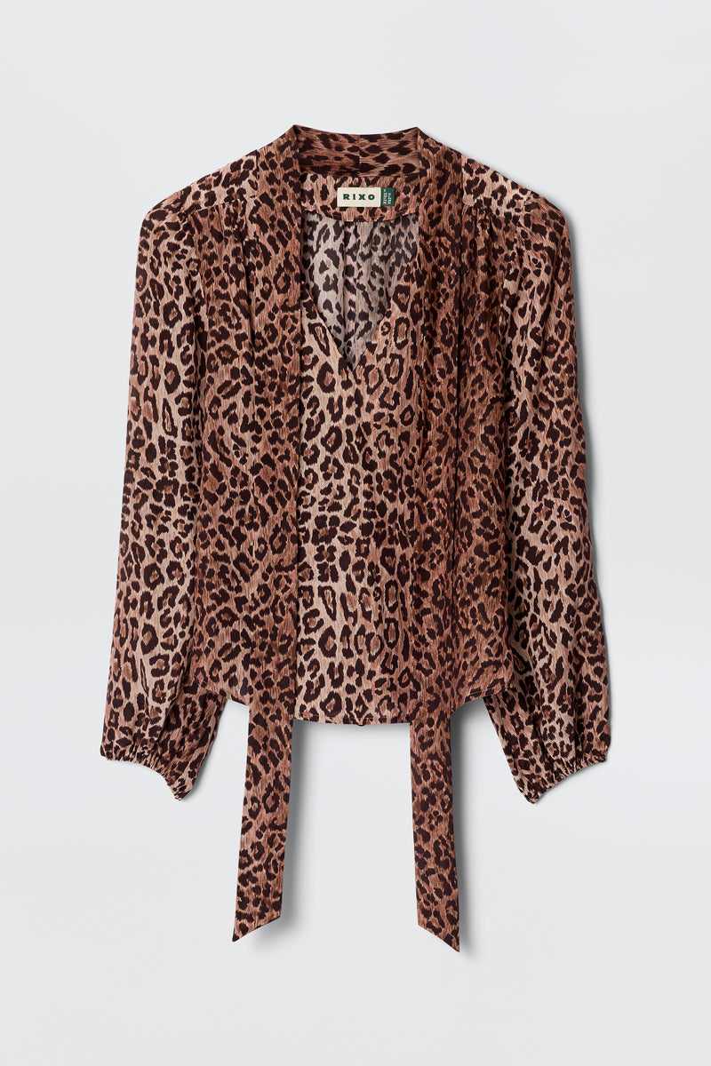 The Moss - Leopard Brown blouse features long sleeves, lightweight leopard-print silk, a V-neck, and front tie details, displayed on a plain light background for a vintage-inspired look.