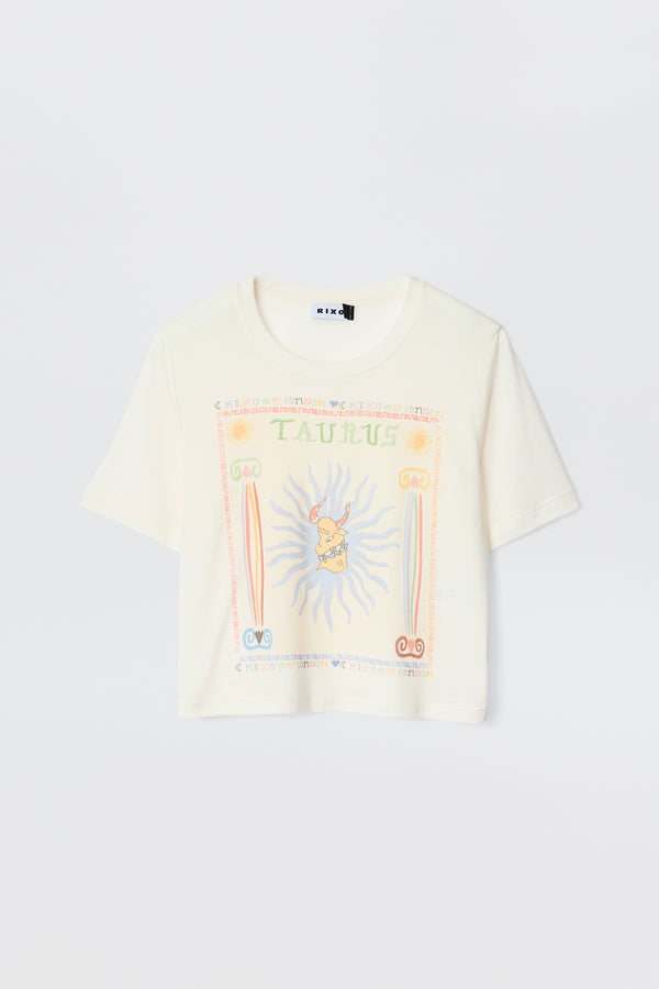 The Ria - Taurus is a cream short-sleeve tee with a vibrant Taurus illustration, astrological symbols, sun rays, and pastel decorative borders—ideal for pairing with RIXO skirts.