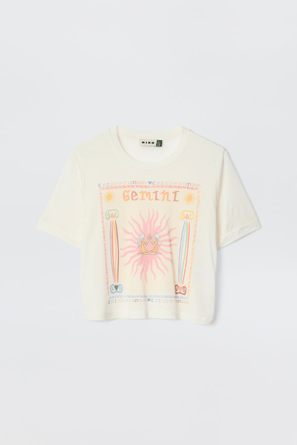 The Ria - Gemini is a white sheer jersey T-shirt with vibrant zodiac-themed graphics, including a bold mirrored Gemini illustration and decorative pink, yellow, blue, and green symbols.