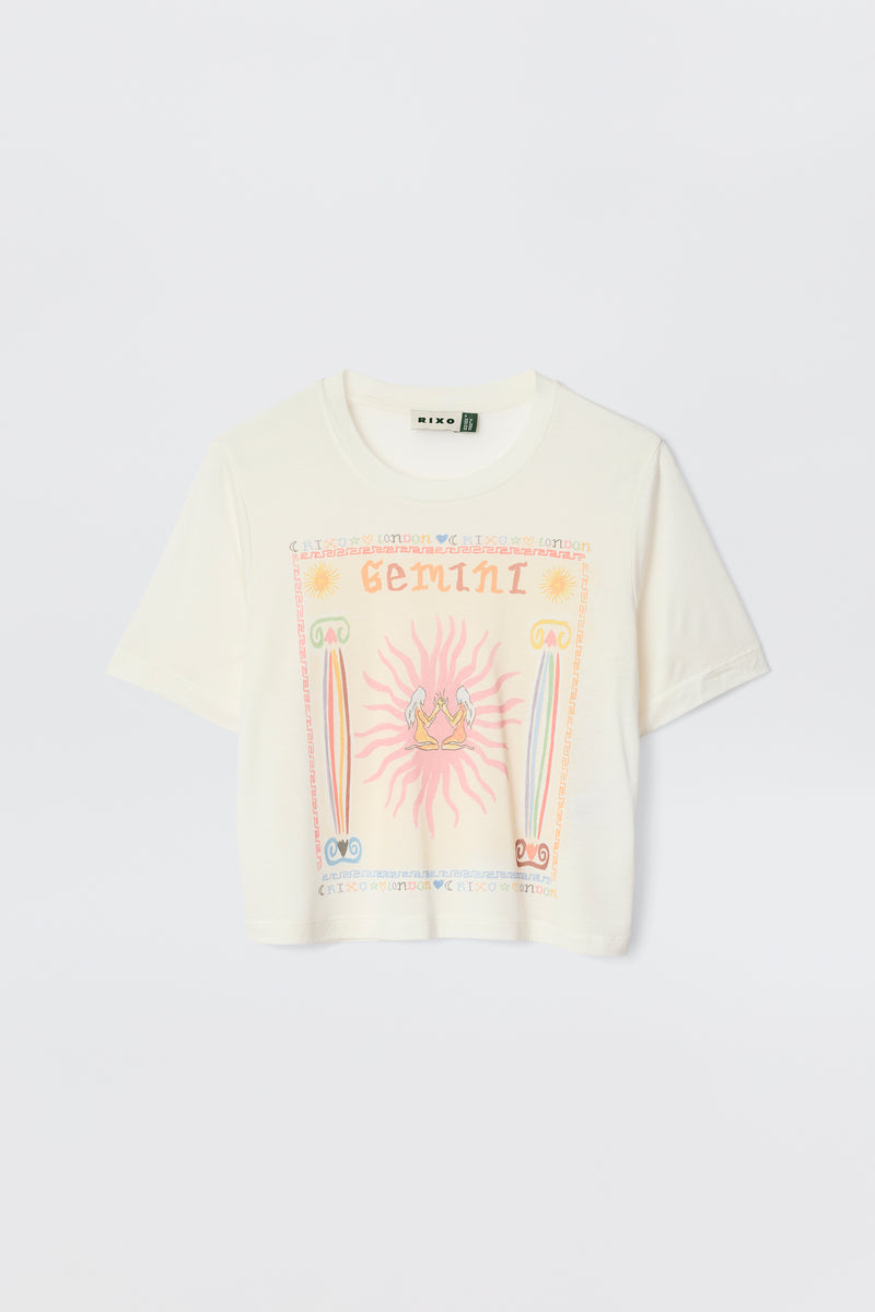 The Ria - Gemini is a white sheer jersey T-shirt with vibrant zodiac-themed graphics, including a bold mirrored Gemini illustration and decorative pink, yellow, blue, and green symbols.