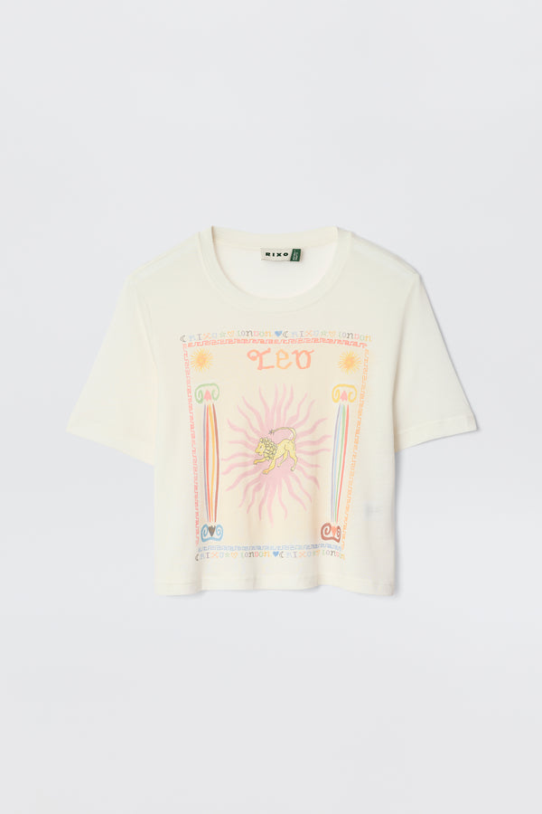 The Ria - Leo is a cream short-sleeve cropped tee with a vibrant Leo graphic—lion, sun rays, "LEO" in orange, and pink, blue, and orange symbols—ideal for pairing with RIXO skirts.
