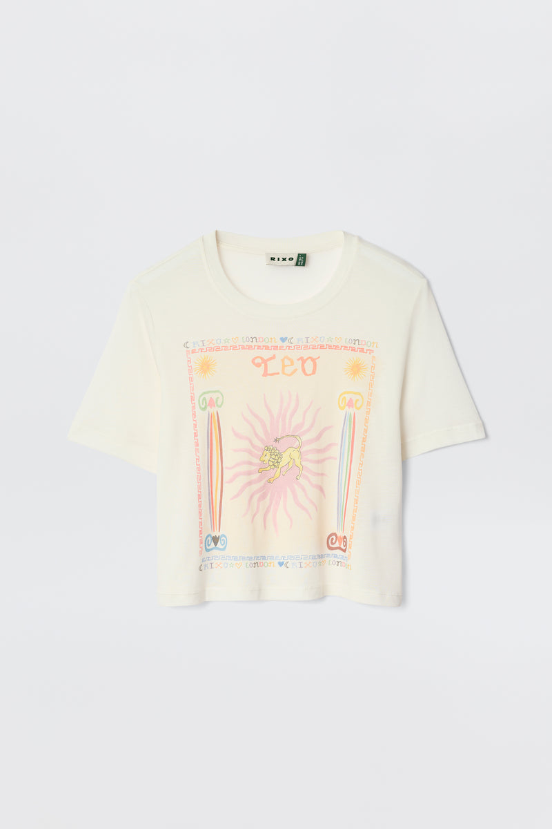 The Ria - Leo is a cream short-sleeve cropped tee with a vibrant Leo graphic—lion, sun rays, "LEO" in orange, and pink, blue, and orange symbols—ideal for pairing with RIXO skirts.