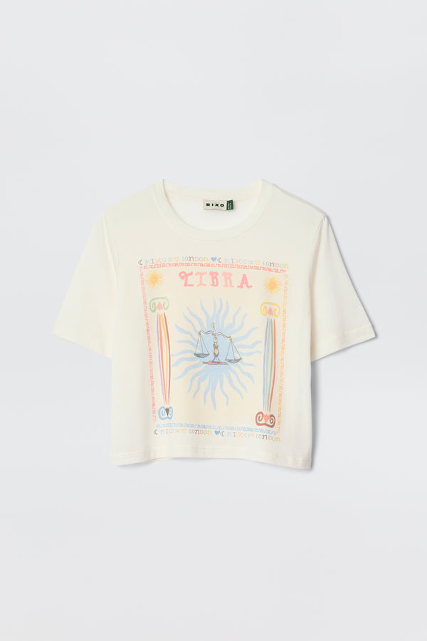 Meet Ria - Libra: a white short-sleeve crop top with a pastel Libra illustration, sunburst pattern, and central scales. Cropped hem for easy pairing with RIXO skirts—perfect for a playful zodiac-inspired look.