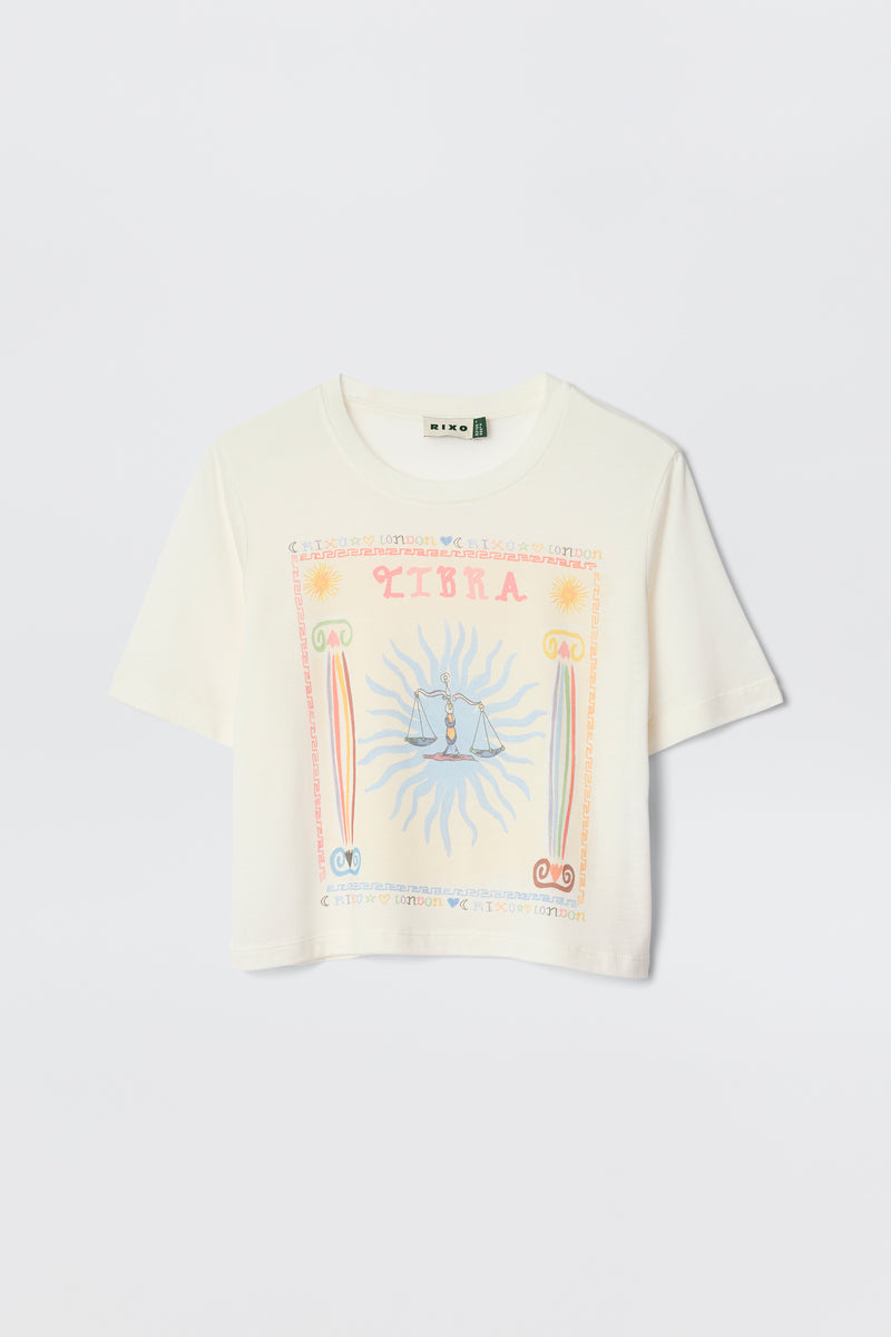 Meet Ria - Libra: a white short-sleeve crop top with a pastel Libra illustration, sunburst pattern, and central scales. Cropped hem for easy pairing with RIXO skirts—perfect for a playful zodiac-inspired look.