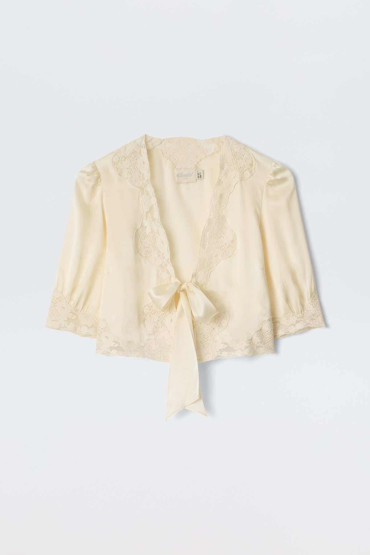The Amara - Champagne is a light cream satin blouse with delicate lace trim, three-quarter sleeves, and a deep V-neckline that ties at the front—ideal for bridal looks or any elegant occasion.
