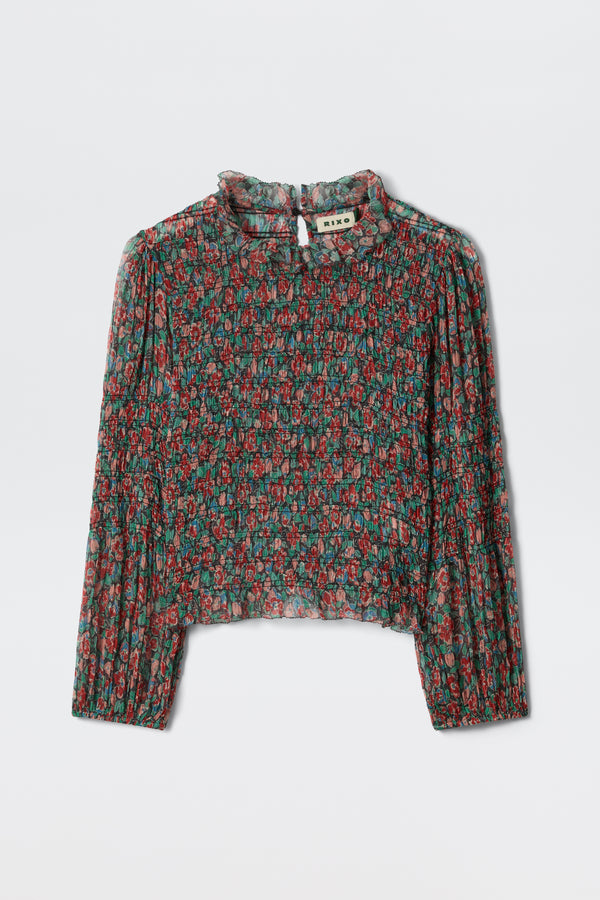The Gardenia - Jeannie Bloom Charcoal is a sheer, long-sleeve blouse with a high ruffled collar and red and green floral pattern on black, shown flat on a white surface.