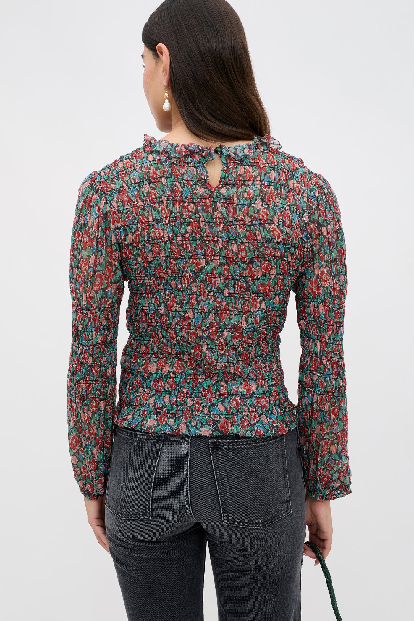 A woman with long dark hair wears the Gardenia - Jeannie Bloom Charcoal floral smocked top and high-waisted black jeans, shown from the back against a plain light background.