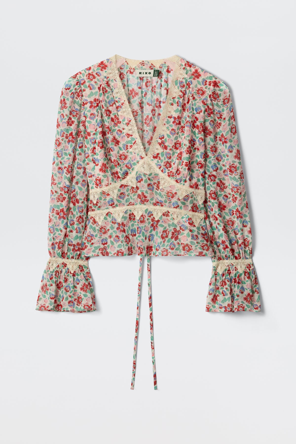 The Lenara - Jeannie Bloom Ivory is a long-sleeved, v-neck blouse featuring a red and blue floral print, lace trim, flared cuffs, and a waist tie, shown against a plain white background.