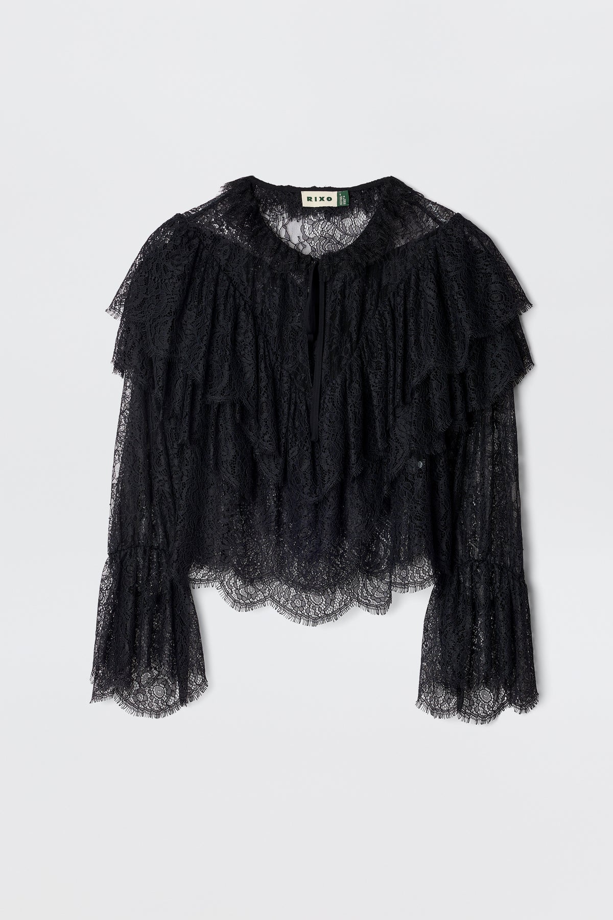 The Faryn - Black is a long-sleeve lace blouse featuring layered ruffles on the chest and sleeves with scalloped hem and cuffs, shown on a plain white background.