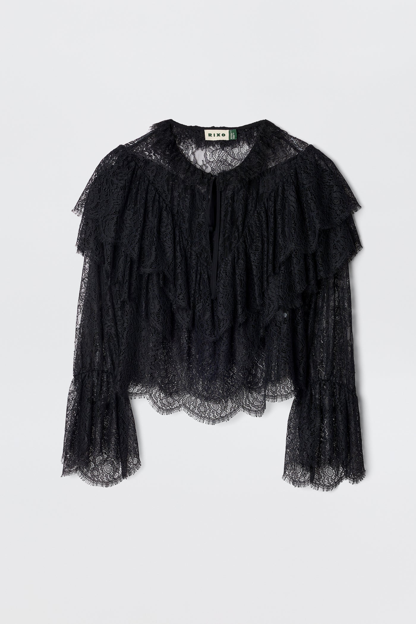 The Faryn - Black is a long-sleeve lace blouse featuring layered ruffles on the chest and sleeves with scalloped hem and cuffs, shown on a plain white background.
