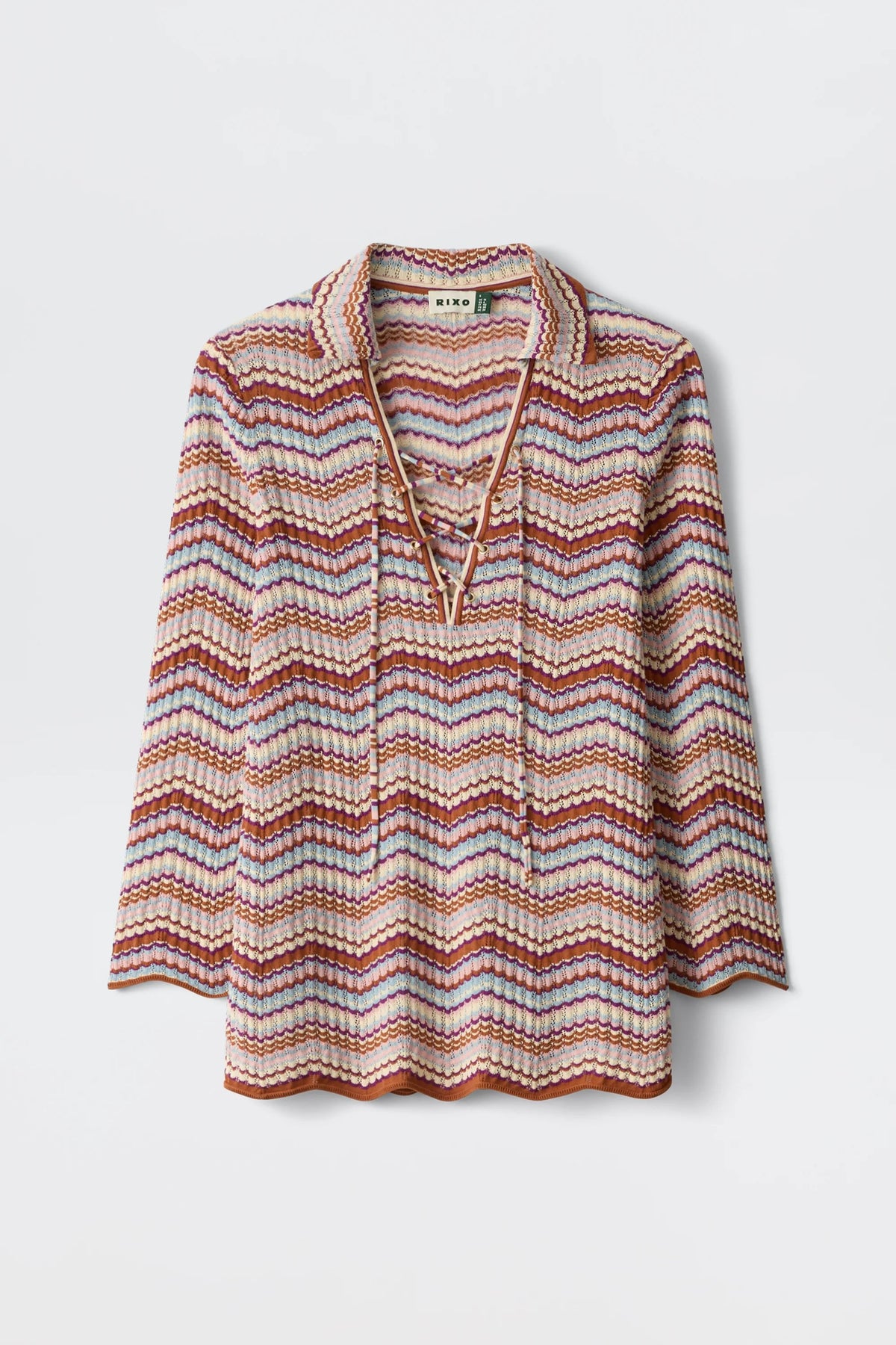 The Brody - Maria Chevron Multi is a vintage-inspired women’s top featuring long sleeves, a collared neckline, and a vibrant pink, purple, and orange chevron pattern. This retro cotton knit piece showcases a charming lace-up V-neck detail and is finished with scalloped edges at the hem and sleeves for an extra touch of playful elegance.
