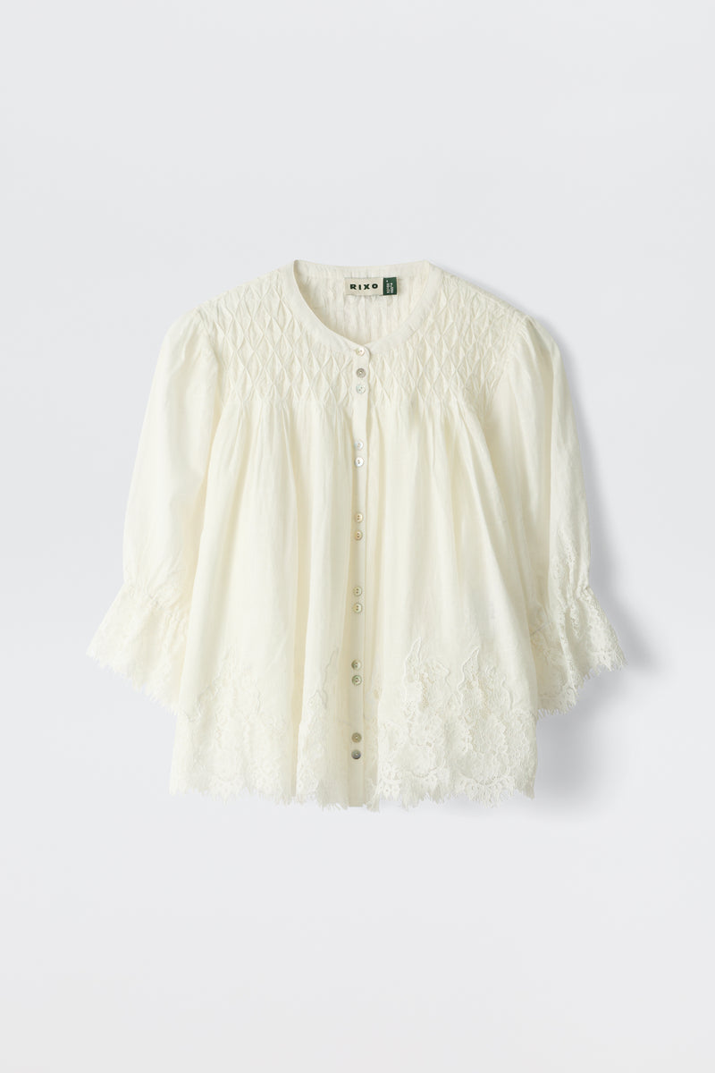 The erika top ivory is a white, long-sleeved blouse featuring a round neckline, button-down front, and delicate lace embroidery on the sleeves and hem. Its lightweight fabric has a subtly textured yoke.