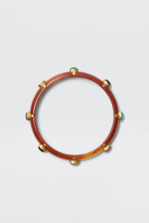 The Sabella - Tortoise is a circular resin bangle in brown with gold-plated accents and multicoloured cabochons spaced around it, shown on a plain light grey background.