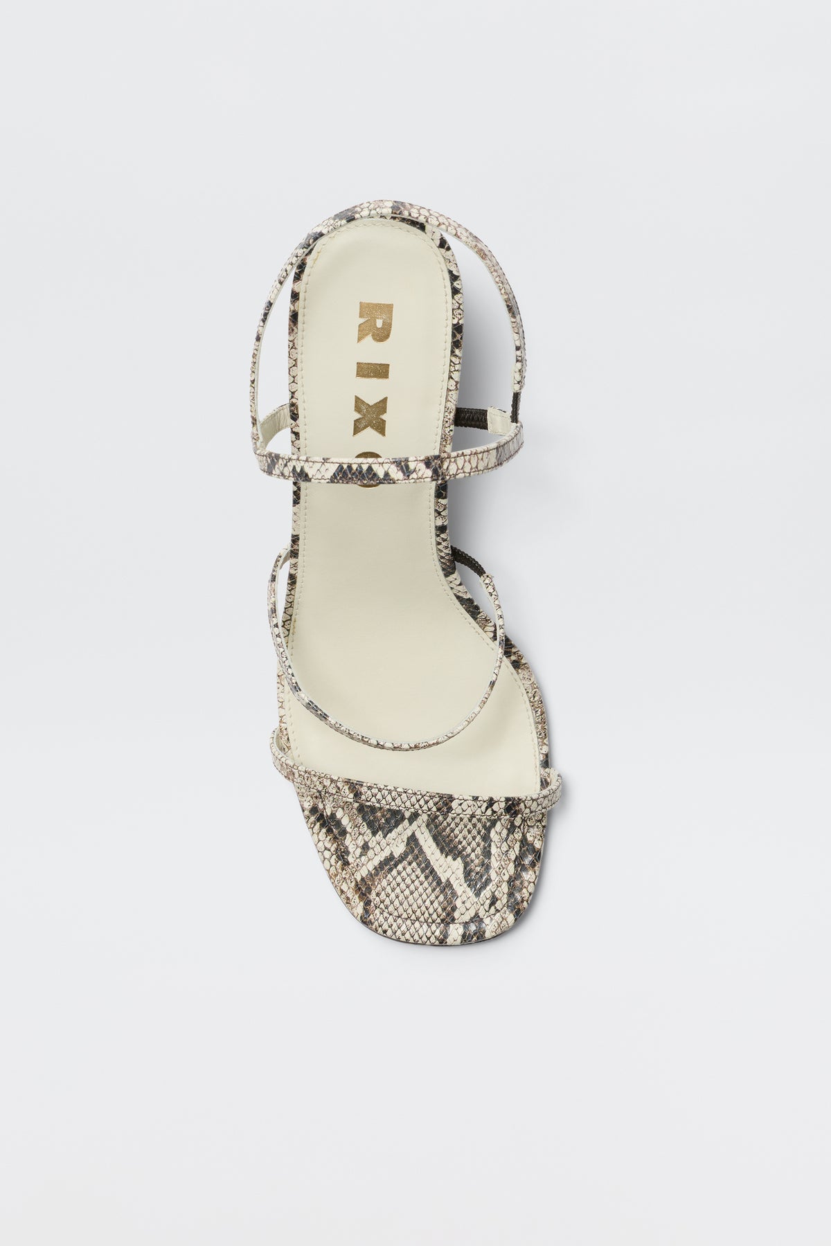 The Ciervo - Snakeskin is a single strappy leather sandal in a beige and black snakeskin print, featuring a square toe and the RIX logo in gold on the insole, displayed against a white background—ideal for complementing your RIXO occasion wear.