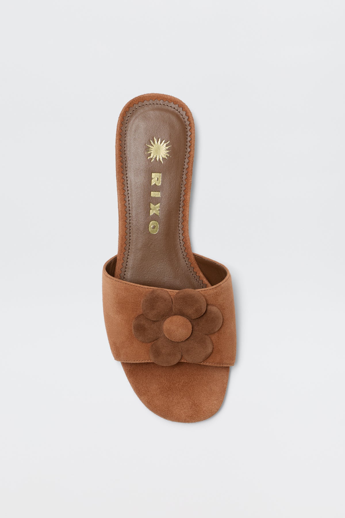 The Kenna - Brown sandals feature a wide brown suede strap with a large, layered flower, and a gold RIXO sunburst logo on the insole. Perfect for summer looks, they're shown on a white background.