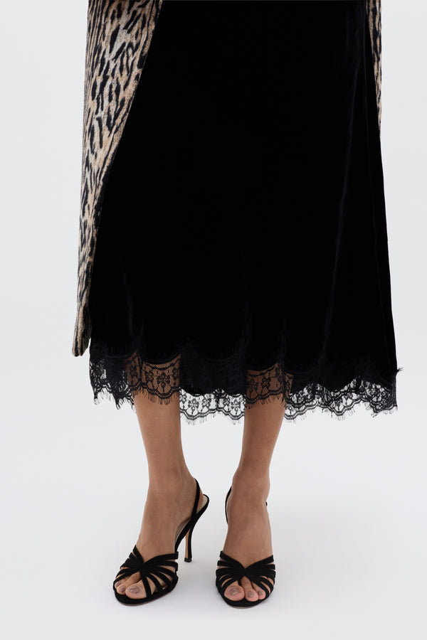 Wearing a black lace-trimmed skirt, glam-heeled Mavi - Black sandals, and a leopard-print coat draped over the shoulders creates a chic and stylish look against a plain background.