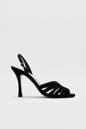 The Mavi - Black high-heeled sandal features an open toe, slim straps, a slingback with gold buckle, and a sleek heel—ideal for adding glamour to any look. Shown against a simple light backdrop.