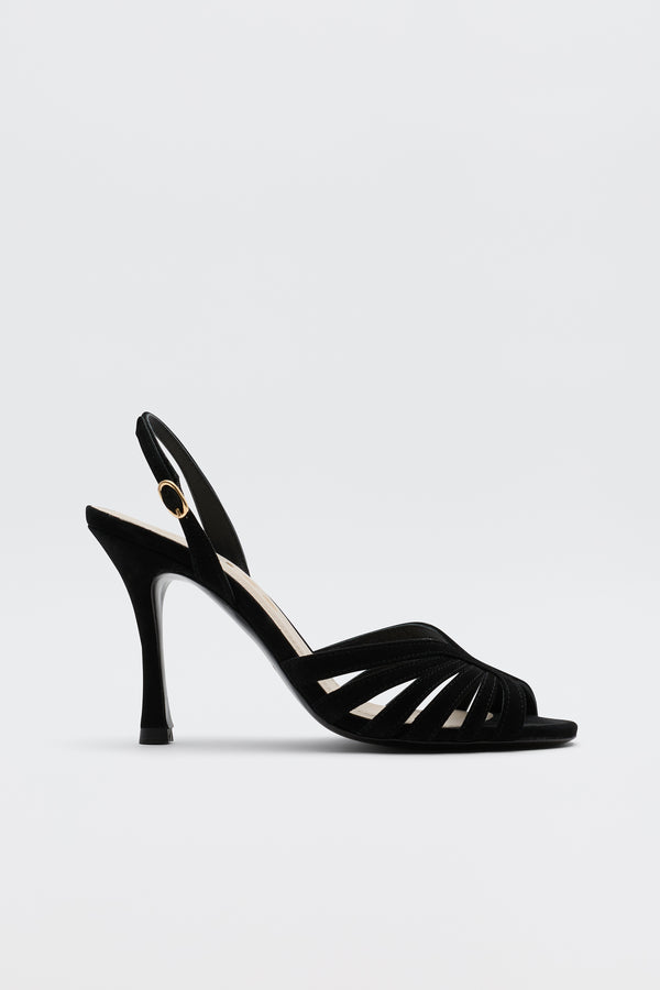 The Mavi - Black high-heeled sandal features an open toe, slim straps, a slingback with gold buckle, and a sleek heel—ideal for adding glamour to any look. Shown against a simple light backdrop.