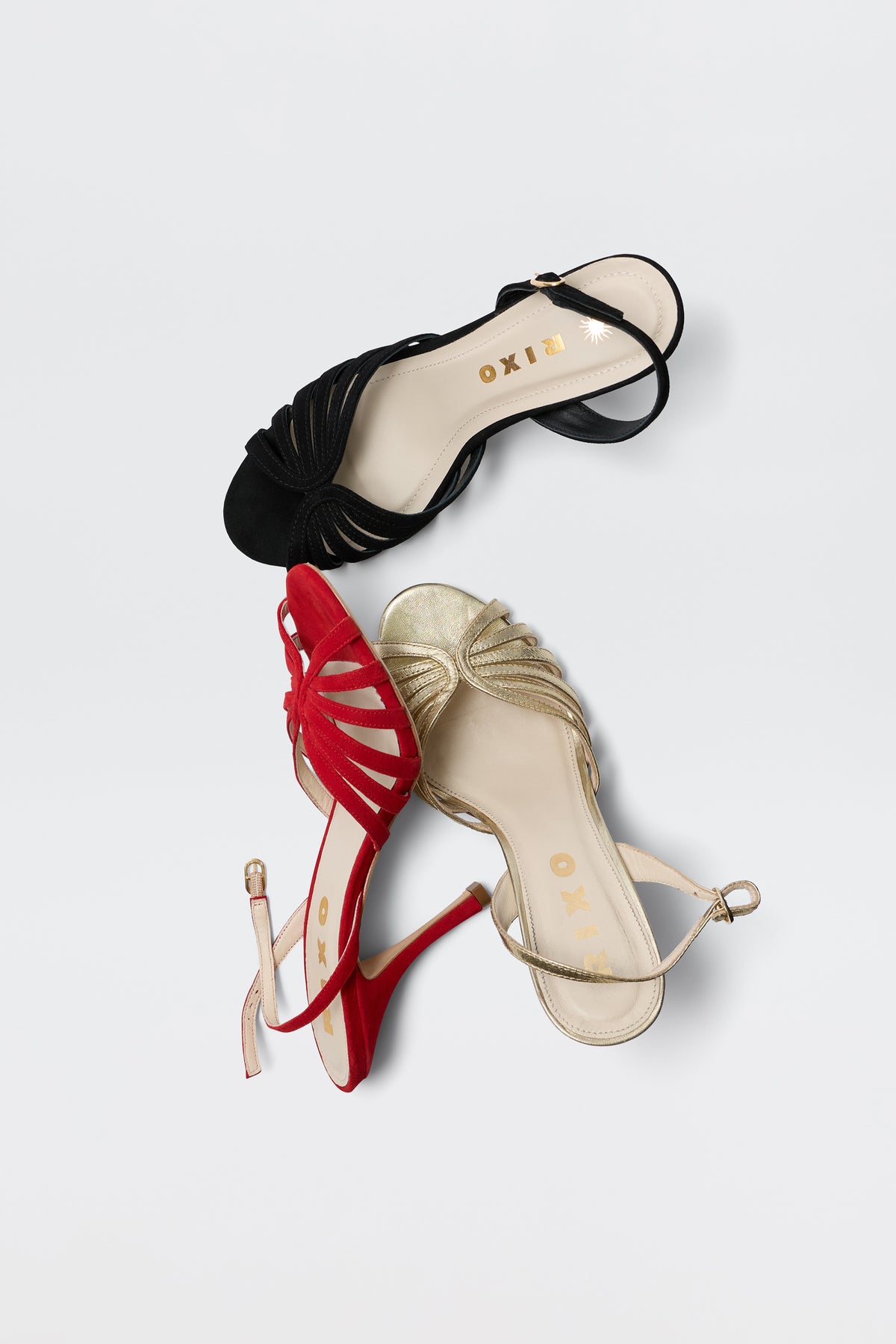 The Mavi - Red sandal from RIXO is a glamorous women's shoe with an open toe, ankle strap, and front knot detail, shown here alongside black and gold variants on a white background. The RIXO logo appears inside each sandal.
