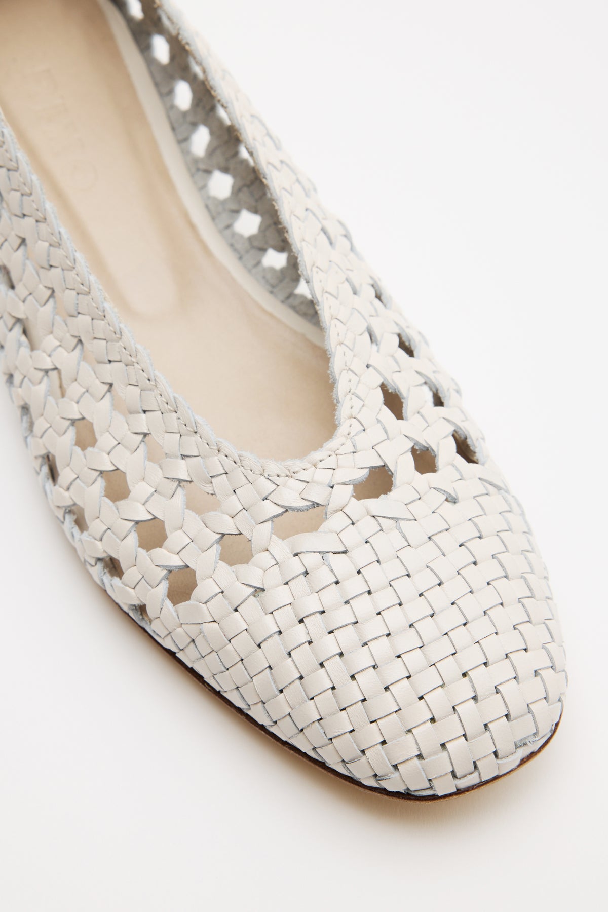 Close-up of the Marlia - Cream: a light-colored woven leather flat with an intricate cut-out pattern and rounded toe, displayed on a plain white background.