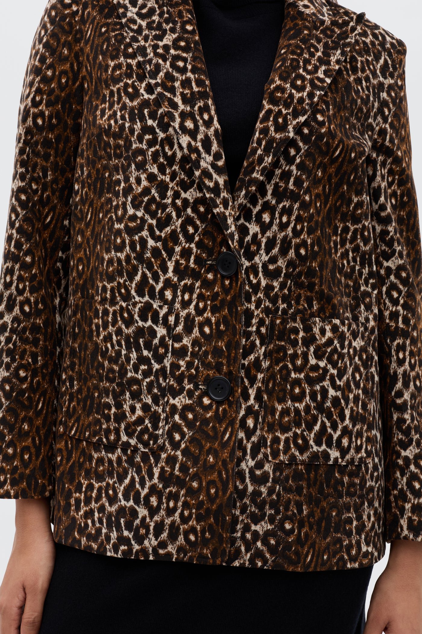 A person wearing the Xander - Lyra Leopard Black jacket, a vintage-inspired blazer in brown and black leopard print with black buttons, notched collar, and front pockets, styled over a black top.