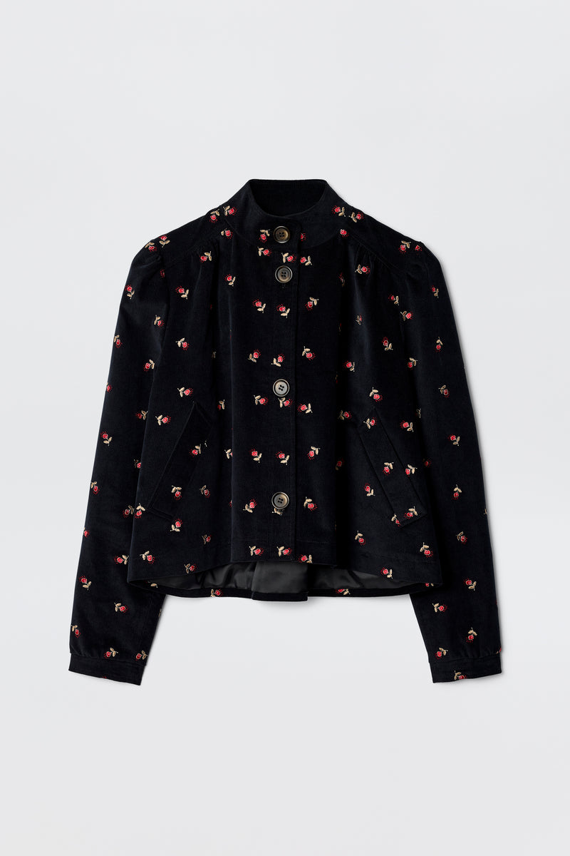 The Nyla - Dandy Embroidery Deep Navy is a 60s-inspired black velvet jacket with long sleeves, a mandarin collar, silver front buttons, and scattered pink and red floral embroidery.