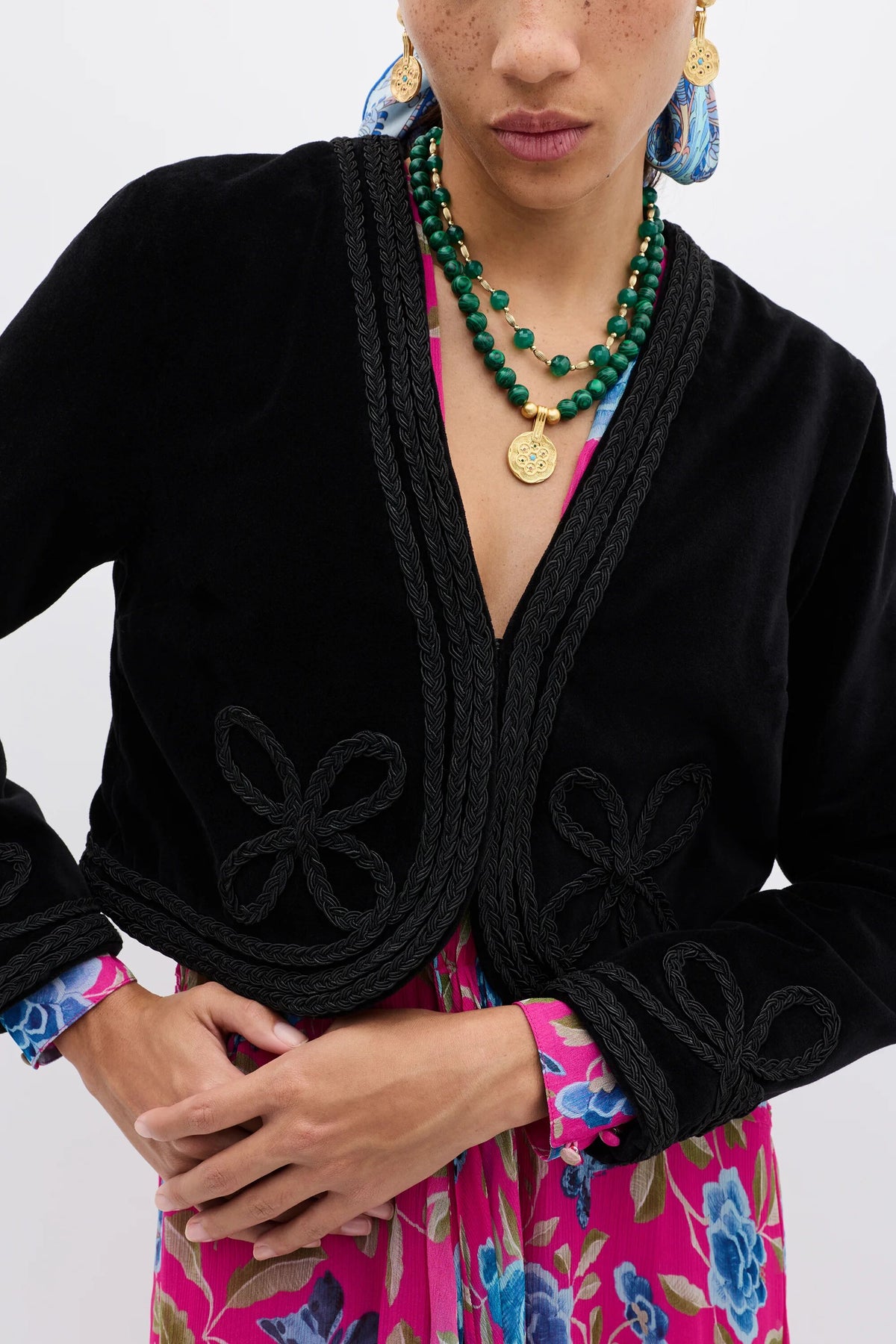 A woman wearing the Kesia - Clover Appliqué Black vintage-inspired jacket and a green necklace.