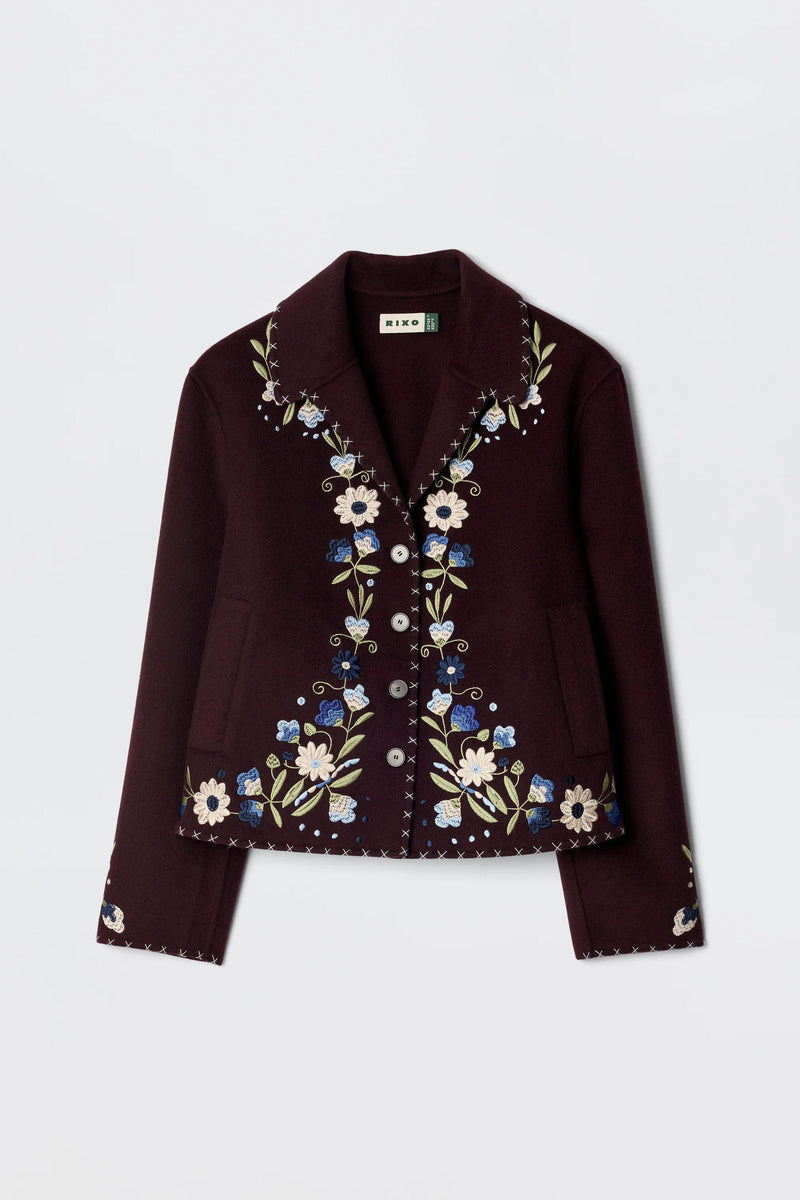 The Jude - Bliss Embroidery Brown jacket is a brown button-up with a collar, detailed with vibrant embroidery in white, blue, and green floral designs along the front, collar, and cuffs for a standout look.