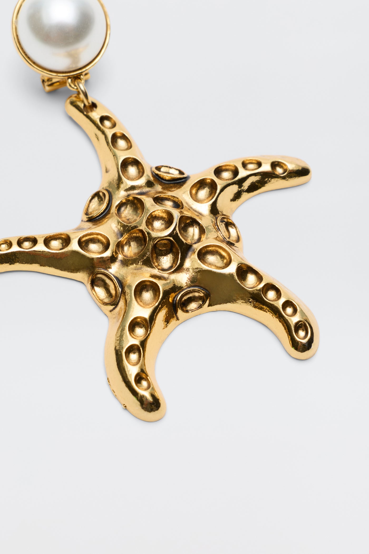The Zeina - Gold pendant features a gold-plated starfish design with raised dots, paired with a round white pearl. Shown on a simple light backdrop, it’s ideal to wear with Zeina earrings or as a standout clip-on piece.