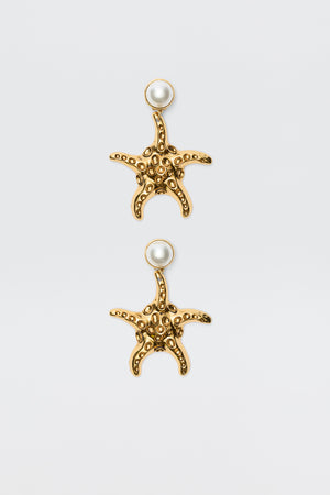 Zeina - Gold earrings featuring starfish shapes with textured surfaces and a round pearl at the top, shown against a plain white background.