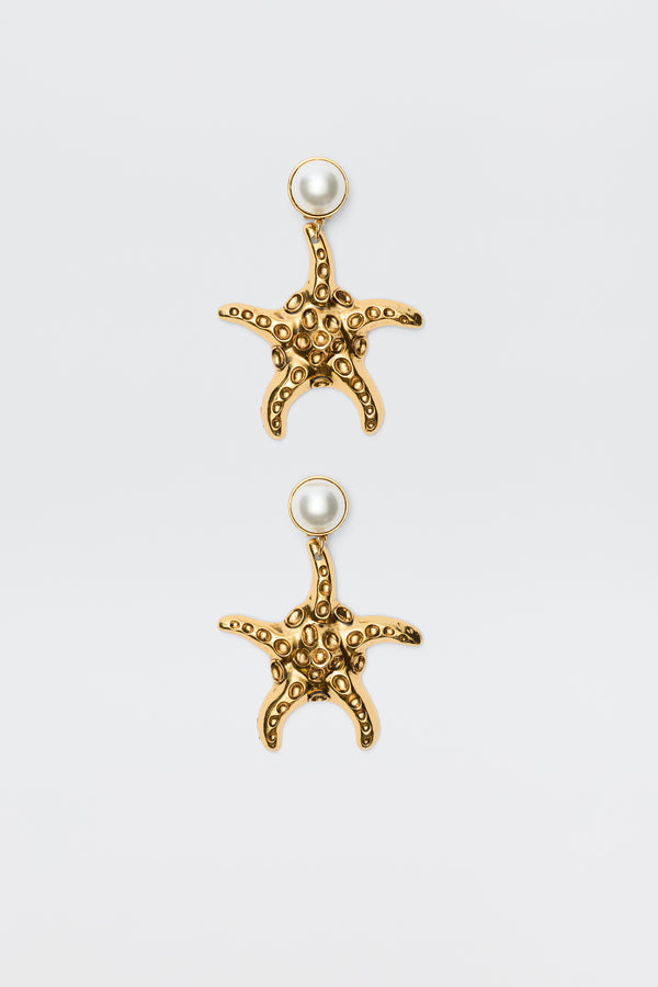 Zeina - Gold earrings featuring starfish shapes with textured surfaces and a round pearl at the top, shown against a plain white background.