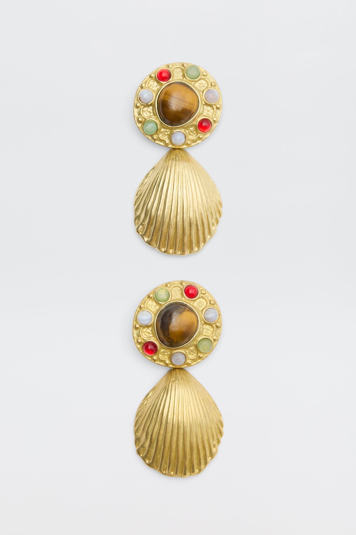 Vixon - Gold: A pair of gold earrings with seashell-shaped danglers, each with a circular top set with green, red, and white stones and a large central brown stone.