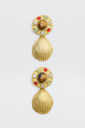 Vixon - Gold: A pair of gold earrings with seashell-shaped danglers, each with a circular top set with green, red, and white stones and a large central brown stone.