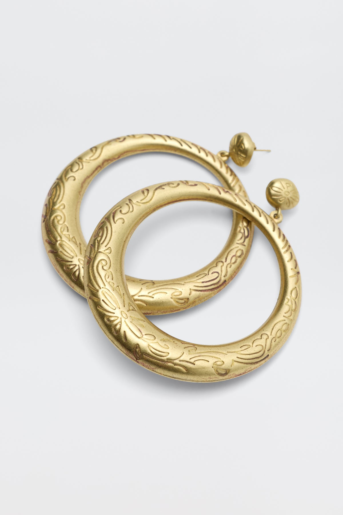 The Sian - Gold earrings are large, round gold pieces with engraved floral and leaf patterns, displayed on a white background.